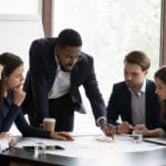 Confident african American male boss work cooperate with diverse team at office briefing, focused biracial businessman head meeting, collaborate discuss business ideas with colleagues at meeting
